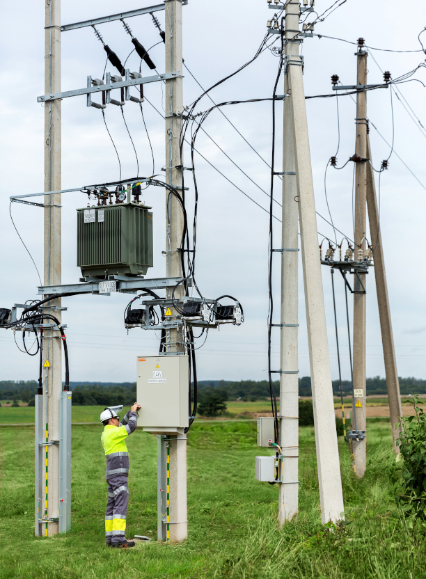 Elektriliinide juures asuv elektrik töötab transformaatori ja puidust postide juures avatud põllul.