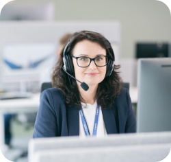 Naine peakomplekti ja mikrofoniga istub arvuti taga, naeratades ja vaadates otse.